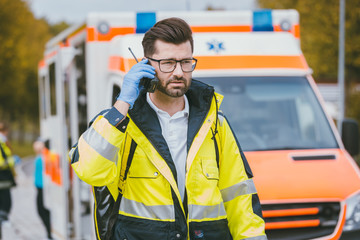 Notarzt Mann spricht mit Einsatzleitung vor dem Krankenwagen