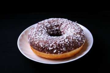 Assorted doughnuts in the glaze, colorful sprinkles and nuts on a black background.