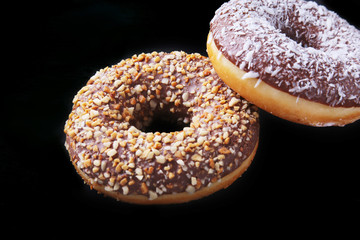 Assorted doughnuts in the glaze, colorful sprinkles and nuts on a black background.