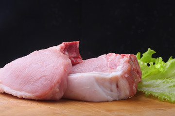 Raw steak on a rustic cutting board with salt, pepper and grinder for spices . Black Background for copy space. Top View.