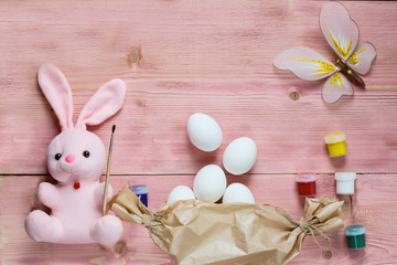 Easter festive set with eggs, flower and easter rabbit, paint, brush, wrapping paper on rustic wooden table with copyspace. Flat lay, space for mock up and copy space. Top view.
