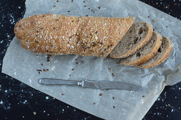 Baguette on a black background. Baguette with seeds and sesame.Baguette with knife. Sliced ​​baguette on the table.