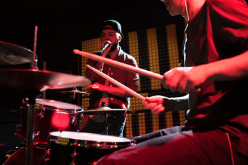 Portrait of hip-hop singer performing with his band in recording studio, drummer in foreground...