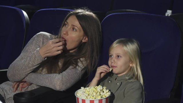 Beautiful woman and her little daughter eating popcorn watching movie at the cinema