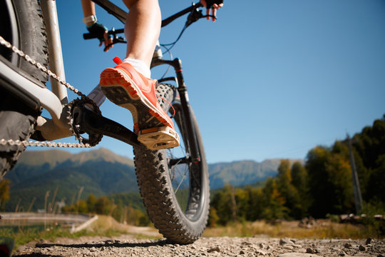 Image of girl in sneakers on bicycle against of mountains
