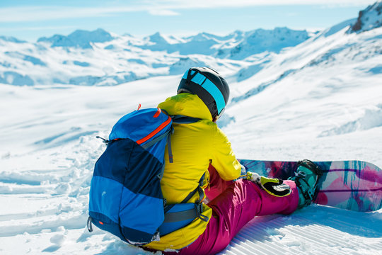 Image from back of woman in helmet with backpack on snow with snowboard
