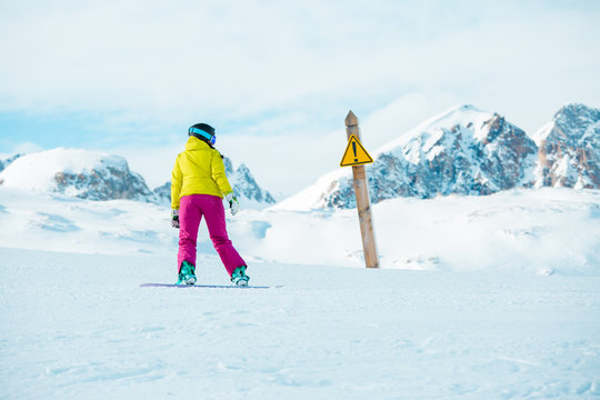 Picture of snowboarder woman wearing helmet at warning sign on mountain