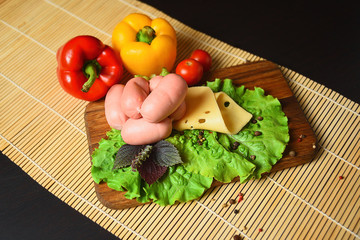 Sausages with cheese on a wooden board with lettuce, basil, cherry tomatoes and paprika.