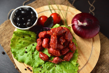Hunting sausages on a wooden board with lettuce, basil, cherry tomatoes, paprika and olives.