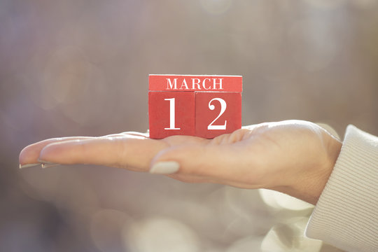 the woman is holding a red wooden calendar. Red wooden cube shape calendar for MAR 12 with hand