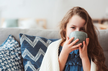 child girl drinking hot tea to recover from flu. Healing kids and protect immunity from seasonal...