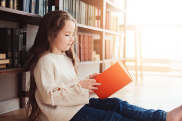 happy smart schoolgirl reading books in library or at home. Kids early learning and education concept.