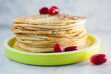 Pancakes with frozen berries pile in a green plate  on a light gray background