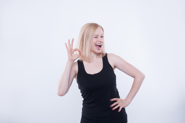 Woman makes ok sign with her hand and beaming. Expressive facial expression and emotion. Portrait of pretty blonde girl smiling isolated on white background.