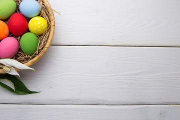 Colored easter eggs on nest beasket with flower on white wooden background top white