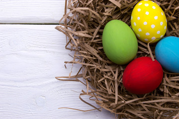 Naklejka na ściany i meble Colored easter eggs in nest top view on white wooden background