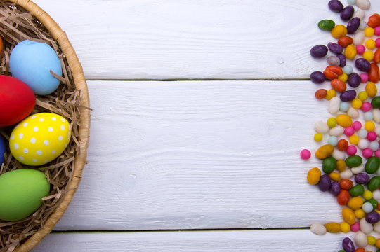 Easter eggs on nest basket and candy top view on white wooden background