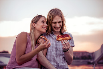 Young couple sitting outdoors and eating pizza