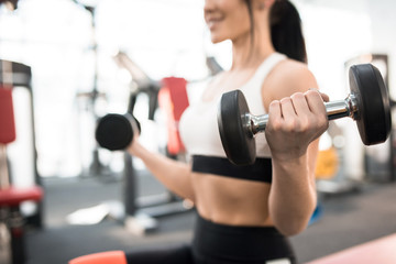 Fototapeta na wymiar Close up of sportive young woman training with dumbbells in modern gym, focus on heavy dumbbell in hand, copy space