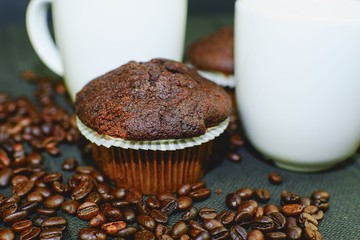 Dark muffins, cups of coffee and coffee beans on black background. 