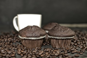 Dark muffin, cups of coffee and coffee beans on black background. Add dark contrasts