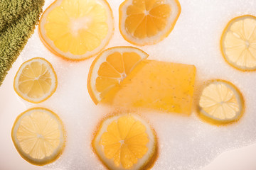 Fototapeta na wymiar yellow lemon glycerine soap in bubbles with fresh slices of lemon and orange