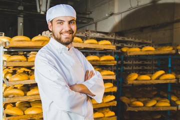 Baker. Bakery. A young handsome worker at a bakery on the background of a rack with ready-made bread. Industrial production of bakery products. a man in a special baker's clothes. Portrait. Working