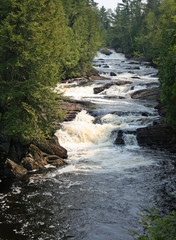 A Maine river pretty much in its natural state, with heavy rapids, whitewater action, deep runs, waterfalls, large pools, flowing through a green forest.