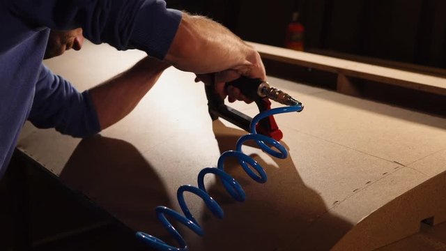 Craftsman is assembling base of furniture in his workplace. He is fixing details of sofa with industrial stapling machine.