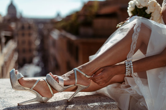 Caucasian bride fastening her silver wedding shoes outdoor