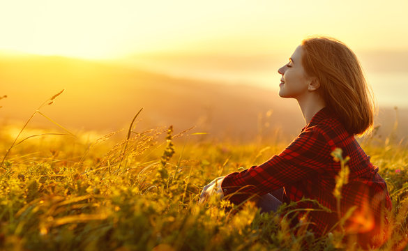 Woman sits with her back in the field and look sunset in the mountains