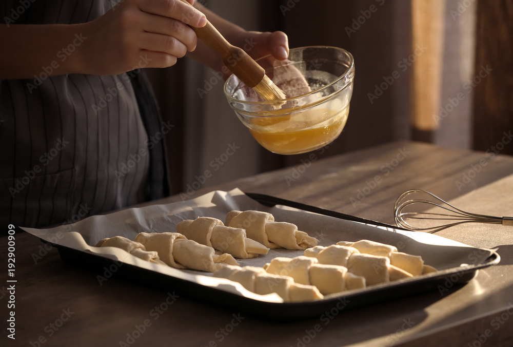 Poster Woman spreading egg yolk onto croissants at table