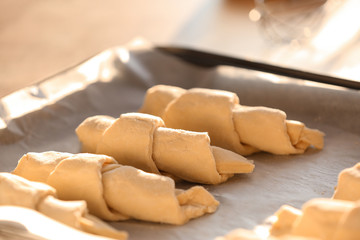 Raw croissants on baking sheet with parchment paper, closeup