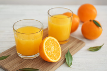 Glasses with fresh orange juice and fruit on wooden board