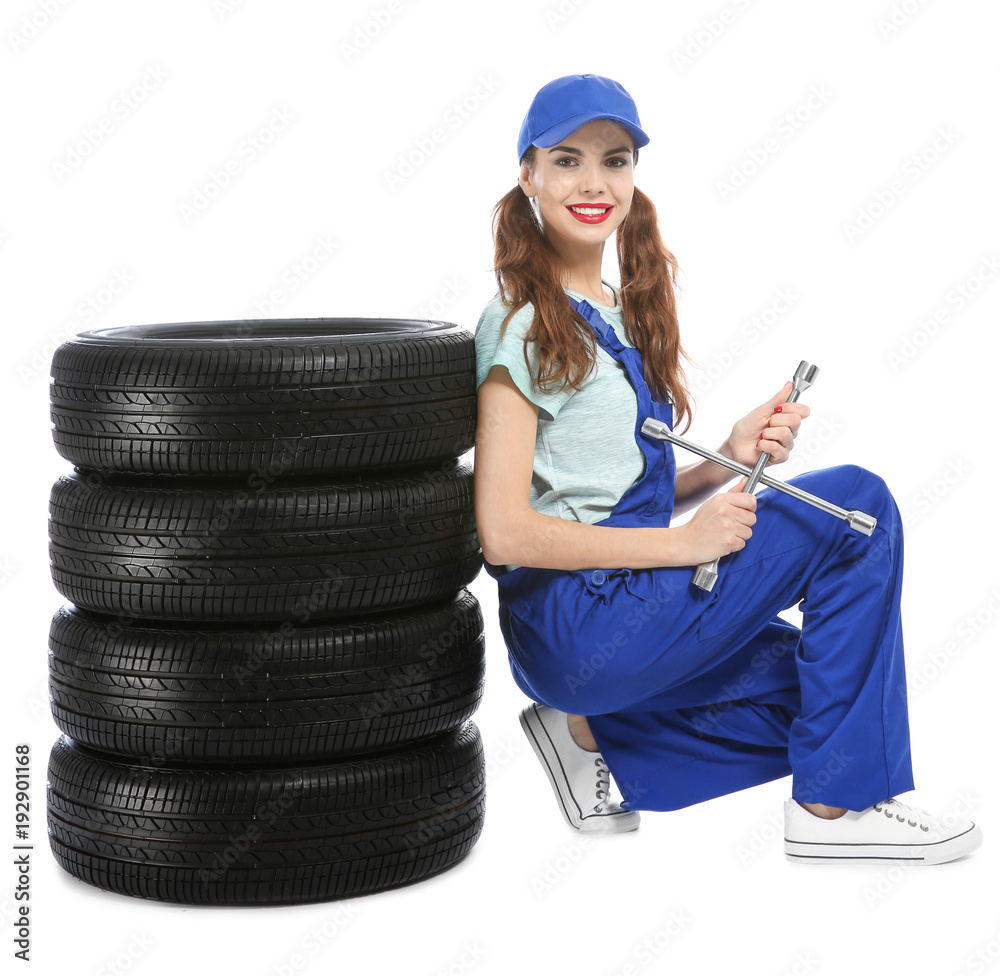 Wall mural Young mechanic in uniform with car tires on white background