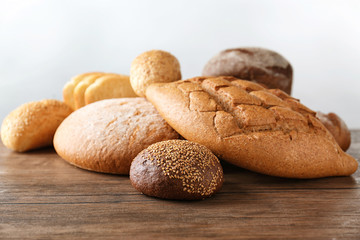 Variety of fresh tasty bread on wooden table against light background