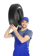 Young mechanic in uniform with car tire on white background