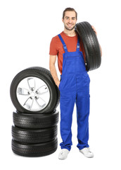 Fototapeta premium Young mechanic in uniform with car tires on white background
