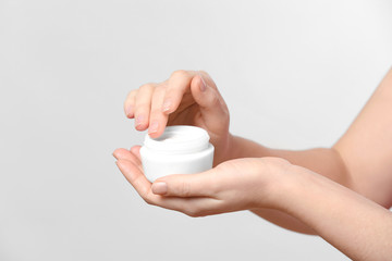 Woman with jar of body cream on light background