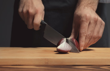Male chef in uniform cutting onion on board, closeup