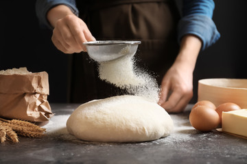 Woman sifting flour over fresh dough on table