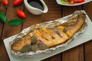Fried fish with fresh tomatoes, herbs and lemon. Wooden background. Top View