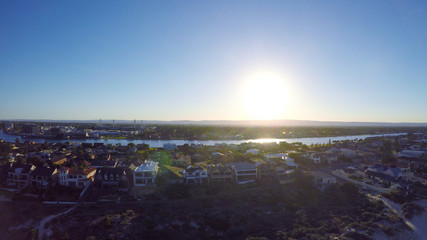 Early morning drone aerial view of South Australian beach with sun rising over Adelaide Hills and West Lakes, and Tennyson homes overlooking the sea.