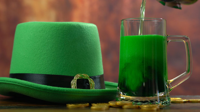 St Patrick's Day pouring green beer with green leprechaun hat and gold covered chocolate coins against rustic wood background