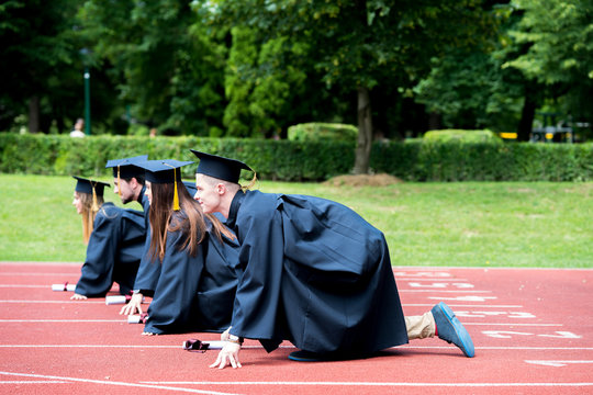 Graduation group of students celebrating on athletic track, preparing to race. Students competiting in a race on athletic track after graduating.