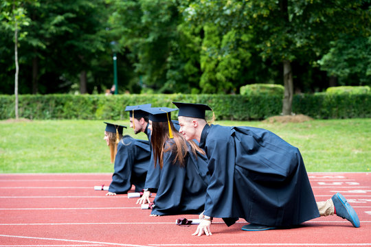 Graduation group of students celebrating on athletic track, preparing to race. Students competiting in a race on athletic track after graduating.