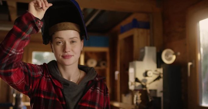Young attractive woman opens her welding helmet and smiles in a workshop