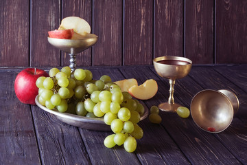 Antique metal goblets with red wine, bunch of grapes and apples,