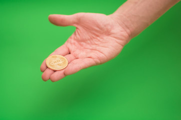 Man's hand holding golden Bitcoin cryptocurrency coin on green background - chroma key / blue box / green screen