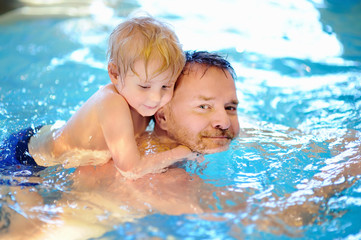 Happy smiling little boy with his father in swimming pool